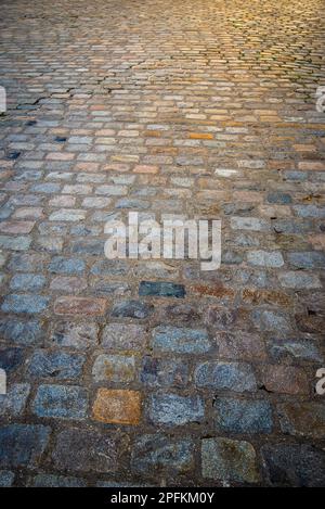 Nahaufnahme von alten mehrfarbigen Kopfsteinen auf der Straße mit Sonnenerscheinungen von oben auf sie herab. Stockfoto