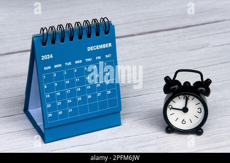 Dezember 2024 Kalender auf Holzschreibtisch und Wecker mit anpassbarem Raum für Text. Monatlicher Kalender und Kopierbereich. Stockfoto