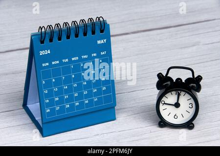 Der Kalender für den 2024. Mai ist mit einem Schreibtisch aus Holz und einem Wecker mit anpassbarem Textbereich ausgestattet. Monatlicher Kalender und Kopierbereich Stockfoto