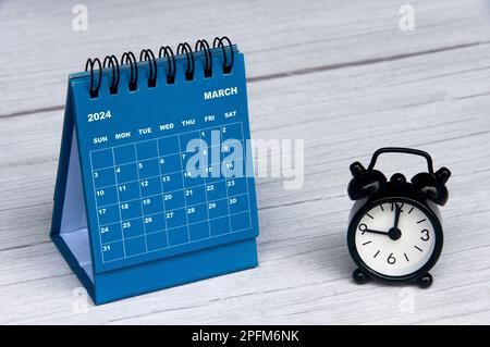 Kalender für März 2024 mit Holzschreibtisch und Wecker mit anpassbarem Raum für Text. Monatlicher Kalender und Kopierbereich. Stockfoto