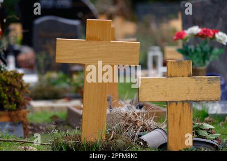 Einfache Holzkreuze auf Gräbern eines Friedhofs vor einem verschwommenen Hintergrund mit Blumen und Grabsteinen Stockfoto