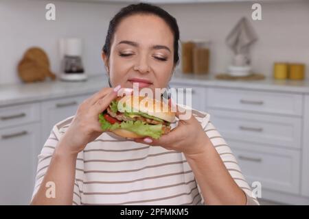Übergewichtige Frau, die zu Hause Burger isst Stockfoto