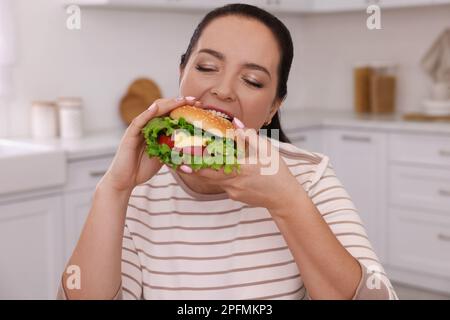 Übergewichtige Frau, die zu Hause Burger isst Stockfoto