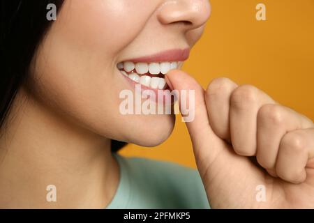 Eine junge Frau, die sich auf gelbem Hintergrund die Nägel biss, Nahaufnahme Stockfoto