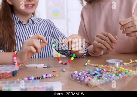 Mutter mit ihrer Tochter, die zu Hause Perlenschmuck herstellt Stockfoto