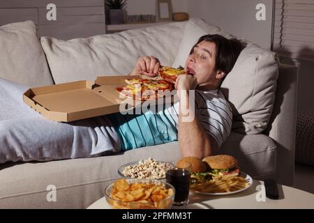 Übergewichtiger Mann, der zu Hause Pizza auf dem Sofa isst Stockfoto