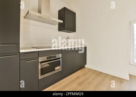 Eine Küche mit Holzfußboden und weißen Wänden in einem Apartment, mit Edelstahlhaube am Herd Stockfoto