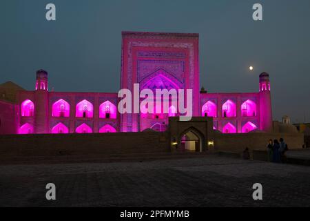 KHIVA, USBEKISTAN - 07. SEPTEMBER 2022: Die antike Madrasa von Allakuli Khan in violetter Nachtbeleuchtung am späten Abend Stockfoto