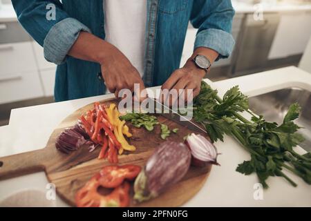 Vorbereitung auf ein gesundes Gericht. Nahaufnahme eines unbekannten Mannes, der Gemüse hackt, während er zu Hause kocht. Stockfoto