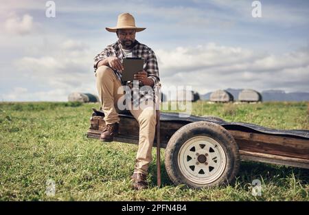 Mitten im Nirgendwo fand die Technologie ihren Platz. Ein erwachsener Mann, der ein digitales Tablet verwendet, während er auf einem Bauernhof arbeitet. Stockfoto