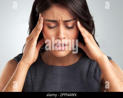 Ich brauche nur eine Pause von allem. Eine junge Frau, die unter Kopfschmerzen leidet, während sie vor weißem Hintergrund steht. Stockfoto