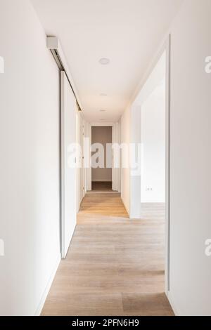 Weißer Korridor mit Eingängen zu einem hellen Raum und Schiebetüren in einem leeren Apartment vor dem Umzug oder nach der Renovierung. Konzept der Renovierung und Stockfoto