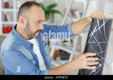 Der Mann klebt die Tapete an die Wand im Haus Stockfoto