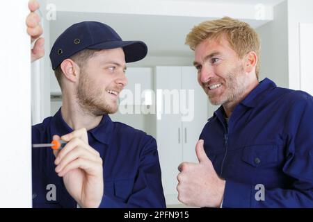 Fröhlicher Boss und lächelnder junger Zimmermann, Türschloss einbauen Stockfoto