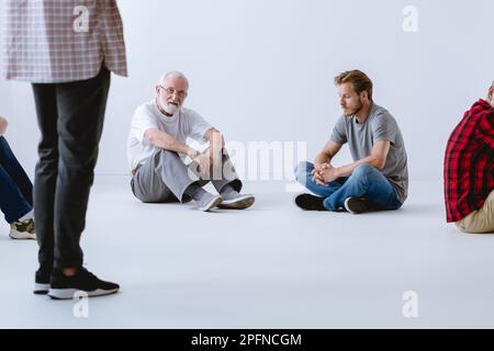 Ein Mann, der vor der Psychotherapie im leeren weißen Raum auf dem Boden saß Stockfoto