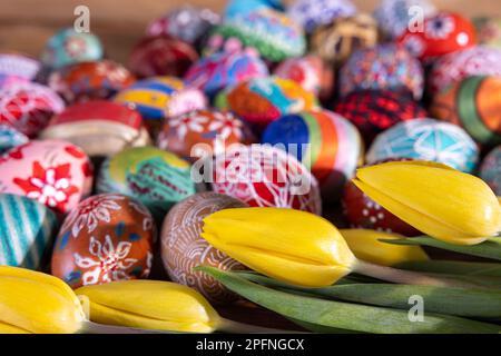 Farbenfrohe Ostereier und gelbe Tulpenblüten füllen den gesamten Rahmen. Stockfoto