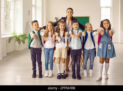 Glückliche Lehrerin umarmt Schüler ihrer Grundklasse. Gruppenfoto für Eltern. Stockfoto