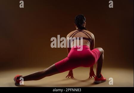 Foto von 30s Frau in der Rückansicht, die sich die Beine streckt. Sie hält am Boden fest Stockfoto