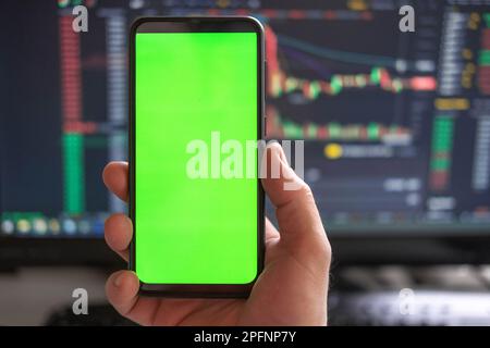 Schwarzes Telefon mit leerem Mockup-Bildschirm auf steigendem Aktiendiagramm. Nahaufnahme-Hand zeigt isoliertes grünes Display des Smartphones. Online-Banking, Nutzung von Fonds-Apps. Fina Stockfoto