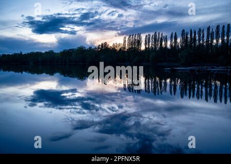 Ein See nach Sonnenuntergang in der blauen Stunde. Ein kleiner Steg und ein paar Boote auf der rechten Seite. Deutschland. Stockfoto