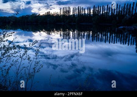 Ein See nach Sonnenuntergang in der blauen Stunde. Ein kleiner Steg und ein paar Boote auf der rechten Seite. Deutschland. Stockfoto