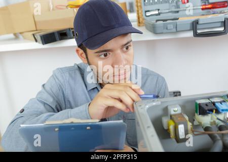 Junger Servicemitarbeiter, der das Gerät untersucht und ein Klemmbrett hält Stockfoto