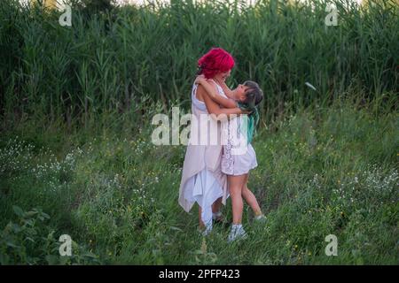 Leuchtend, vielfältig, außergewöhnliche Mutter und Tochter, die sich im Wald umarmen. Die Frau hat rosa Haare, das Mädchen hat grüne Haare. Zärtliche Mutterschaft, glückliches Chi Stockfoto