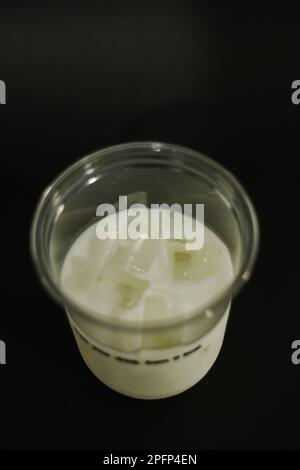Milch und Eiswürfel in einem Kunststoffglas auf schwarzem Hintergrund Stockfoto