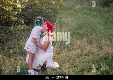 Leuchtend, vielfältig, außergewöhnliche Mutter und Tochter, die sich im Wald umarmen. Die Frau hat rosa Haare, das Mädchen hat grüne Haare. Zärtliche Mutterschaft, glückliches Chi Stockfoto