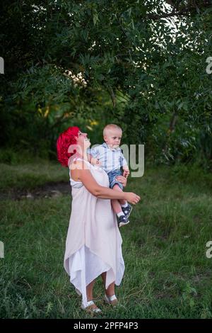 Portrait von Bright, Diversität, außergewöhnliche Mutter und kleiner Sohn umarmen den Wald. Die Frau hat rosa Haare. Zärtliche Mutterschaft, glückliche Kindheit. Res Stockfoto