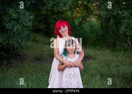 Leuchtend, vielfältig, außergewöhnliche Mutter und Tochter, die sich im Wald umarmen. Die Frau hat rosa Haare, das Mädchen hat grüne Haare. Zärtliche Mutterschaft, glückliches Chi Stockfoto