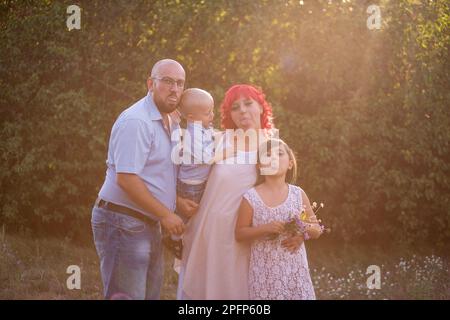 Eine bunte Familie, die herumspielt und ihre Zunge auf grünem botanischem Hintergrund zeigt. Kahlköpfiger Vater mit Brille umarmt kleinen Sohn, Mutter mit rosa ha Stockfoto