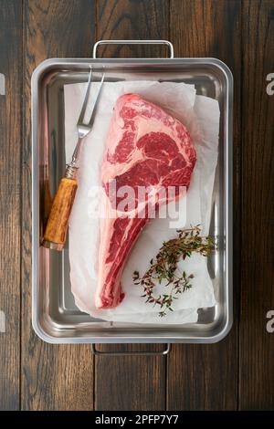 Frisches rohes Tomahawk-Steak. Trocken gereiftes rohes Tomahawk-Rindersteak mit Kräutern und Salz auf altem Holzhintergrund. Grillvorgang wird vorbereitet. Draufsicht und Kopierbereich. Stockfoto