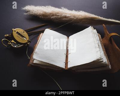 Tagebuch oder Tagebuch aus Vintage-Leder auf einem schwarzen Tisch mit einem Kompass daneben Stockfoto