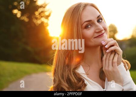 Süßes blondes Mädchen im Hintergrund der Sonne. Gewöhnliche glückliche Frau, die das Leben im Sommer genießt. Selbstbewusster Mensch Stockfoto