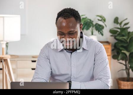 Fokussierter afrikanischer Geschäftsmann mit Dokumenten, der sich ein Notebook ansieht und recherchiert. Business Financial Analyst Konzept Stockfoto