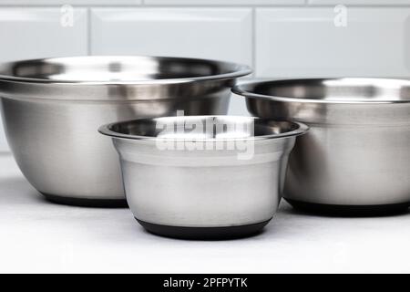 Set mit 3 Edelstahlschüsseln. Jede Schüssel hat eine andere Größe. Küchenzubehör auf einem hellen Tisch. Stockfoto