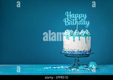 Weißer Tropfkuchen mit blauer Ganache, Streuseln und einem Happy Birthday Topper auf blauem Hintergrund. Einfach und trendig. Speicherplatz kopieren. Stockfoto