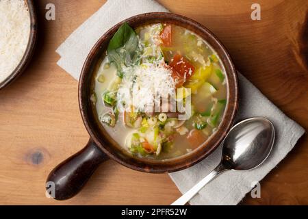 Italienische Minestrone-Gemüsesuppe mit Bohnen und Pasta in einer rustikalen Terrakotta-Schüssel Stockfoto