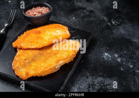 Gebratene panierte Tilapia-Filets auf einem Marmorbrett. Schwarzer Hintergrund. Draufsicht. Speicherplatz kopieren. Stockfoto