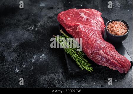 Rohes amerikanisches Tri-Tip-Rindfleisch auf Marmorbrett. Schwarzer Hintergrund. Draufsicht. Speicherplatz kopieren. Stockfoto