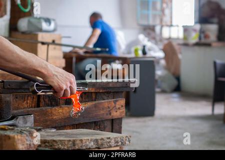 Traditioneller Glasbläser, der Flüssigglas formt. Details und Nahaufnahme eines Arbeiters, der Flüssigglas in einer Glasfabrik formt. Handgefertigt, farbig Stockfoto