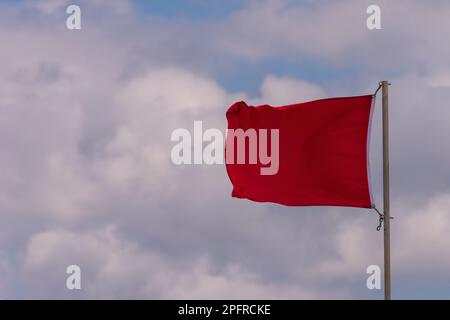 Eine rote Warnfahne am Strand flattert im Wind. Stockfoto