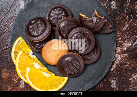 Ein Stapel schokoladenüberzogener runder Jaffa-Kekse mit Marmelade mit Orangengeschmack. Dunkler Hintergrund. Draufsicht. Stockfoto