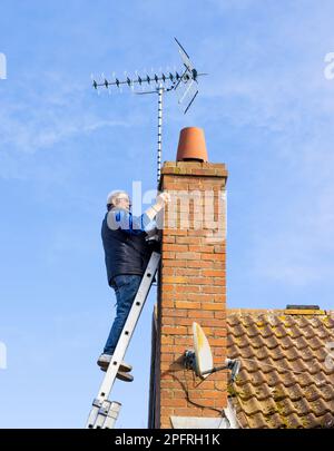 Ein Mann, der eine neue Fernsehantenne auf einem Schornsteinstapel installiert. UK Stockfoto