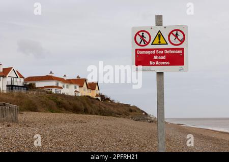 Ein Schild auf Thorpeness Beach warnt die Öffentlichkeit vor beschädigten Meeresschutzanlagen, mit Gebäuden und Klippen im Hintergrund, die nicht im Fokus sind. UK Stockfoto