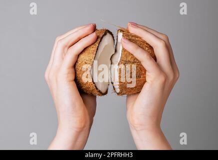 Hände öffnen Kokosnuss, zwei Hälften Kokosnussfrucht in brauner Schale. Stockfoto