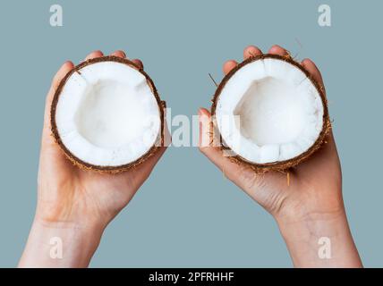 Hände halten zwei Kokosnussteile. Querschnitte von Kokosnussfrüchten mit reifem weißem Fleisch. Stockfoto