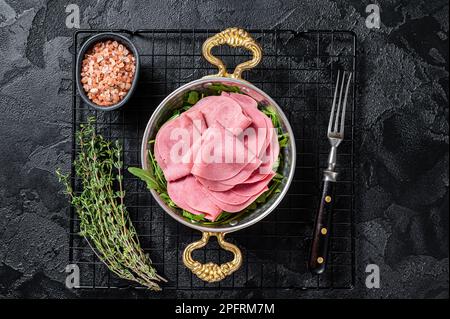 Dünne Schinkenscheiben in einer Pfanne mit Rucola-Salat. Schwarzer Hintergrund. Draufsicht. Stockfoto