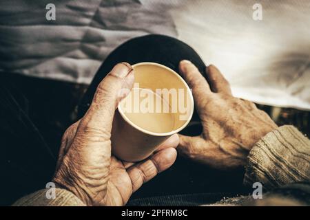 Von oben, anonymer älterer Mann, der einen Pullover trägt, sitzt mit einer beigen Papptasse Kaffee Stockfoto